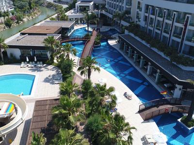Modern hotel pool area with bridges, palm trees, and lounge chairs surrounded by buildings.