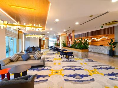 Bright hotel lobby with modern furniture, soft carpet, and reception desk with plants.