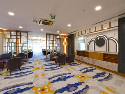 Modern hotel lobby with colorful carpet and comfortable armchairs under bright ceiling lights.