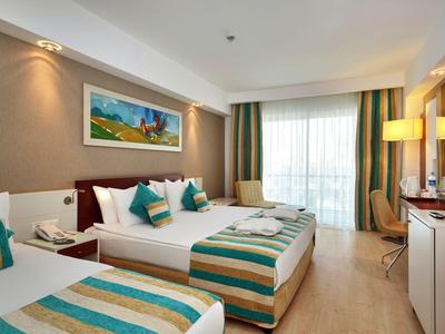 Bright hotel room with two beds, modern furniture, and large windows with curtains.