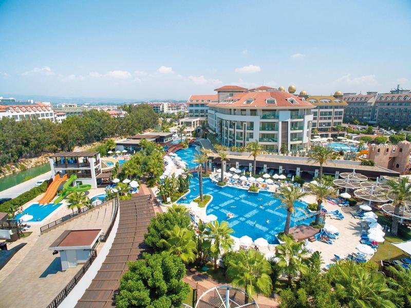 Große Hotelanlage mit mehreren Pools, Palmen, Sonnenschirmen und modernen Gebäuden am Meer.