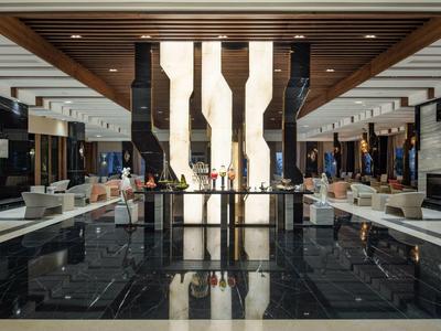 Große Hotellobby mit schwarzem Marmorboden, weißen Sitzgruppen und moderner Holzdeckenverkleidung.