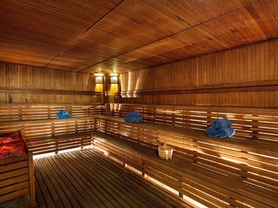 Innenraum einer Holzsauna mit Bänken, warmem Licht und blau-roten Handtüchern.