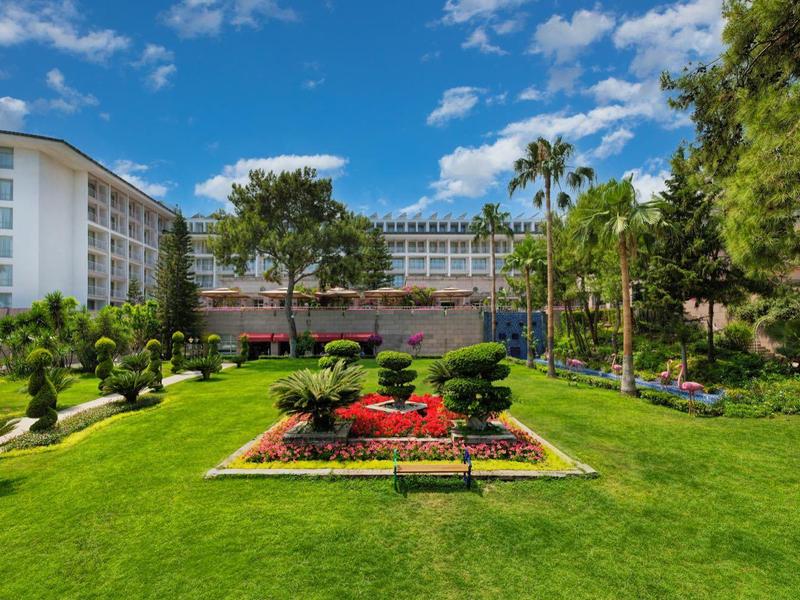 Zadbany ogród z zieloną trawą i kolorowymi kwiatami przed nowoczesnym hotelem.