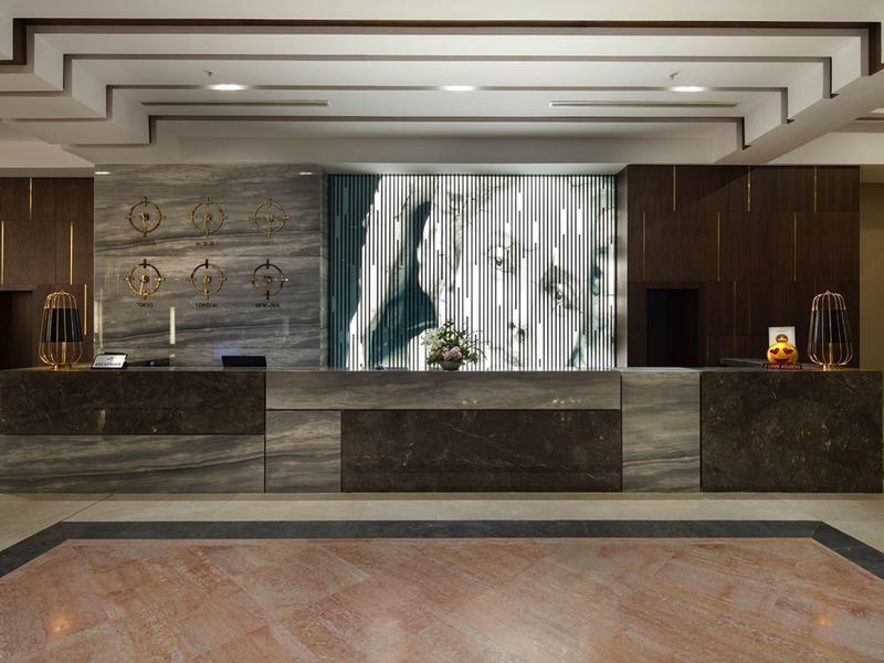 Nowoczesna recepcja hotelowa z marmurowymi ladami i dekoracyjną ścianą.