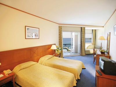 Camera d'hotel con due letti singoli, balcone e vista sul mare.