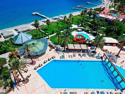 Grande piscina accanto a giardino tropicale e spiaggia in hotel con mare blu.