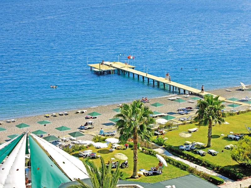 Spiaggia con lettini, palme e un molo che si estende nel mare blu.