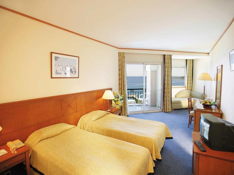 Camera d'hotel luminosa con due letti singoli e balcone con vista mare.