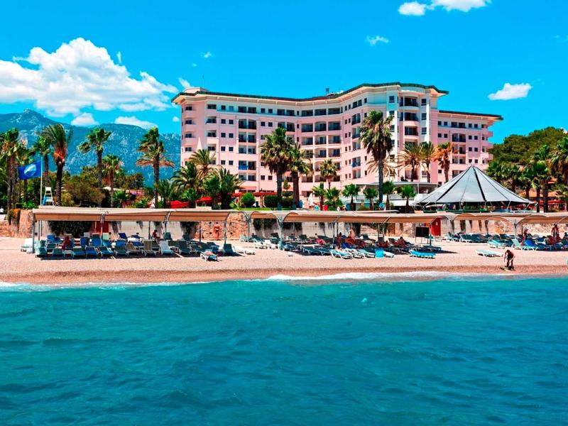 Spiaggia con palme, ombrelloni e un grande edificio alberghiero sullo sfondo sotto un cielo sereno.