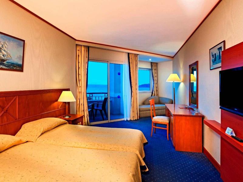 Camera d'hotel con due letti, balcone e vista sul mare al crepuscolo.