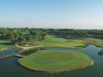 Rozlehlé zelené golfové hřiště s jezírky a mosty pod jasnou oblohou.