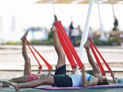 People doing stretching exercises with red bands on yoga mats outdoors by the water.
