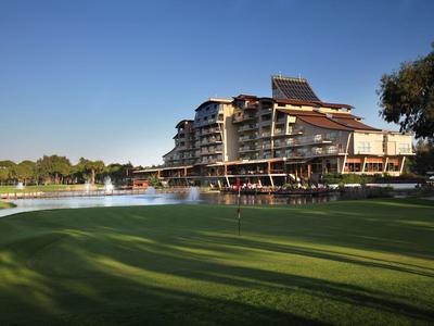 Moderní hotel se sluneční terasou vedle zeleného golfového hřiště pod modrou oblohou.