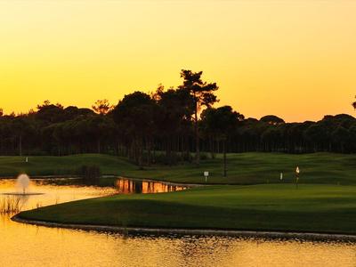 A peaceful golf course at sunset with water hazards and trees in the background.