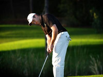Golfer in white pants and black shirt putting on green golf course.