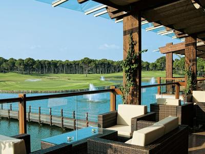 Terrassenbereich mit bequemen Sitzmöbeln, Holzsäulen und Blick auf einen Golfplatz und Teich.