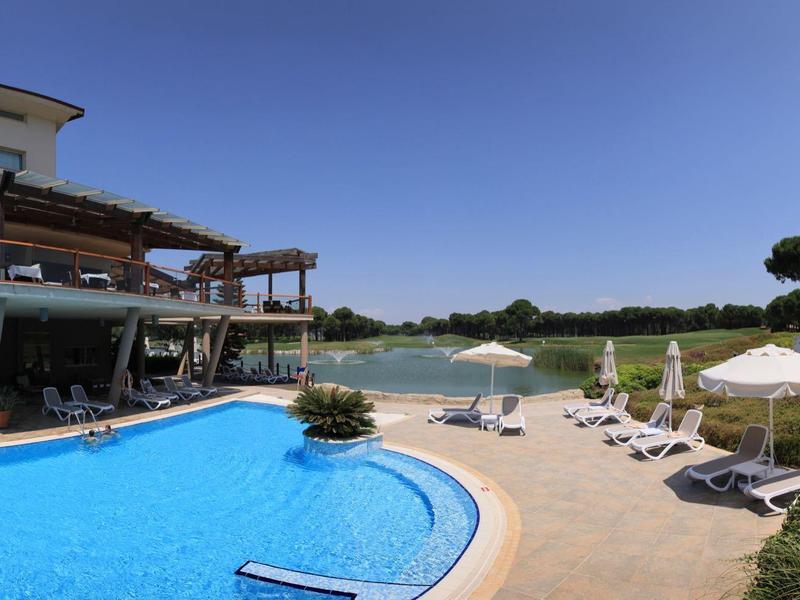 Moderní hotelový bazén s deštníky, lehátky a jasně modrou oblohou.