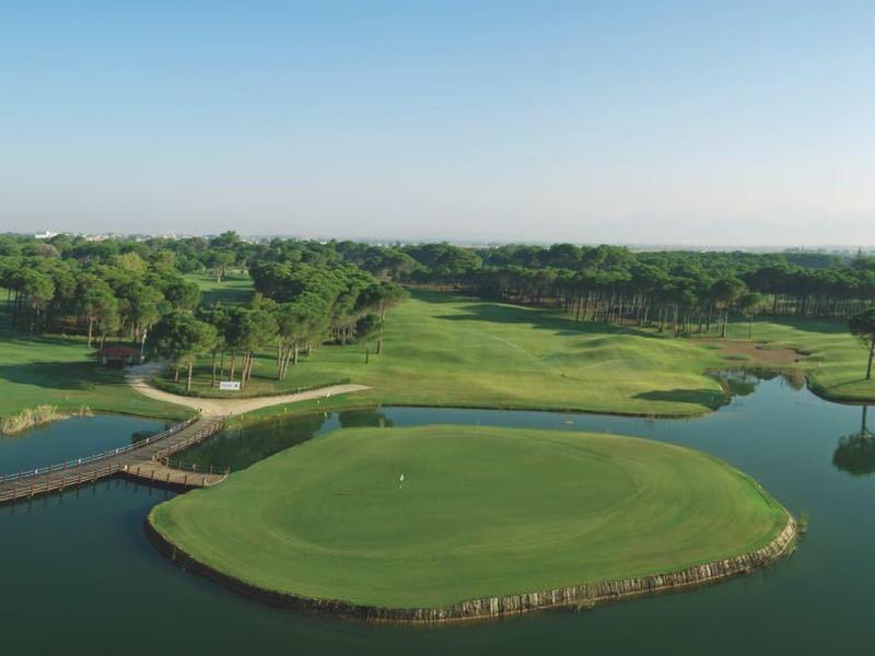 Rozlehlé zelené golfové hřiště s jezírky a mosty pod jasnou oblohou.