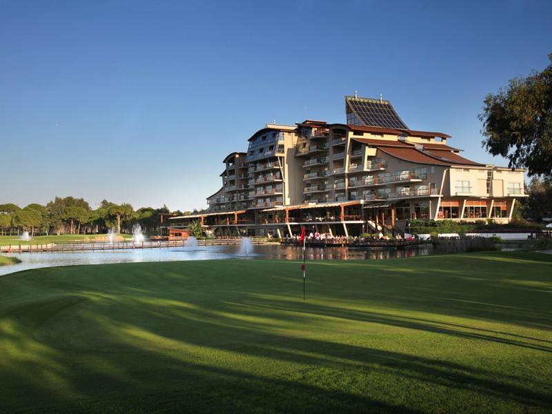 Moderní hotel se sluneční terasou vedle zeleného golfového hřiště pod modrou oblohou.