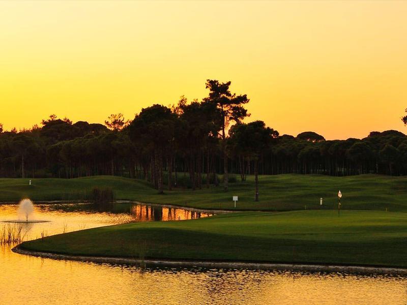 Golfové hřiště při západu slunce s vodou a zelenými trávníky.