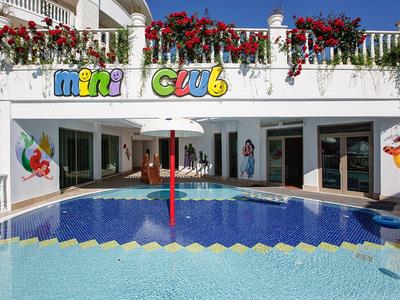 Vnitřní bazén s dětským klubem v světlém hotelu s květinami na terase