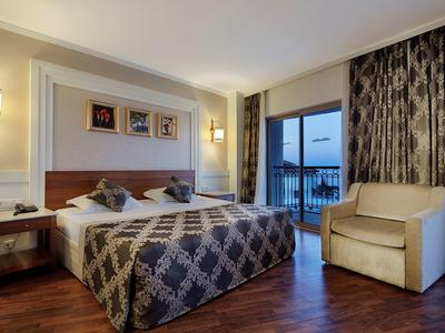 Hotelzimmer mit Doppelbett, Nachttischen, Sessel, Vorhängen und Balkon mit Aussicht.