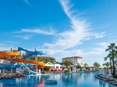 Grande piscina con scivoli d'acqua e sdraio sotto un cielo blu in un resort.