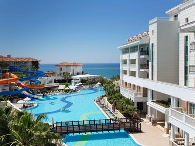 Hotel con grande piscina, scivoli d'acqua e vista sul mare sotto un cielo limpido.