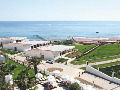 Pohled z hotelu na pláž s palmami a bílými slunečníky.