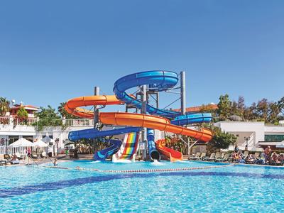 Groot buitenzwembad met kleurrijke glijbanen en ligstoelen in hotelgebied bij zonnig weer.