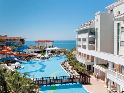 Hotel s velkým bazénem, vodními skluzavkami a výhledem na moře pod jasnou oblohou.