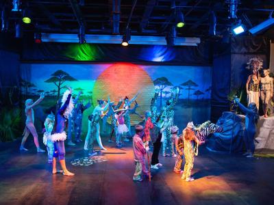 Barevné divadelní představení s herci v kostýmech na osvětleném jevišti.