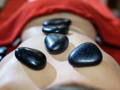 Černé horké kameny na zádech osoby během wellness masáže.