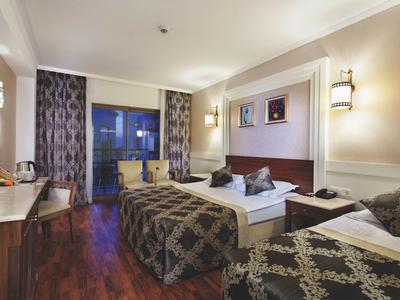 Světle zařízený hotelový pokoj s manželskou postelí, křeslem a dřevěnou podlahou.