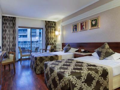 Moderně zařízený hotelový pokoj s manželskou postelí, psacím stolem a balkonem.