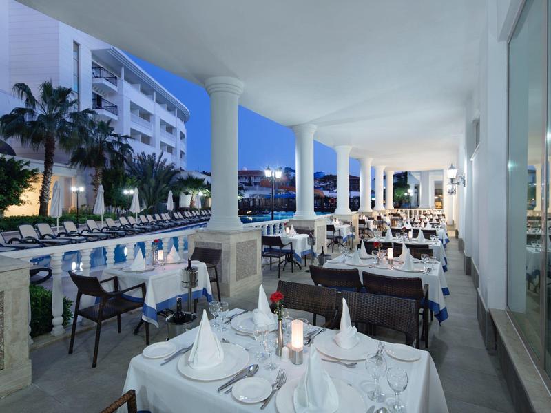 Hotelová terasa s prostřenými stoly a výhledem na osvětlený bazén za soumraku.