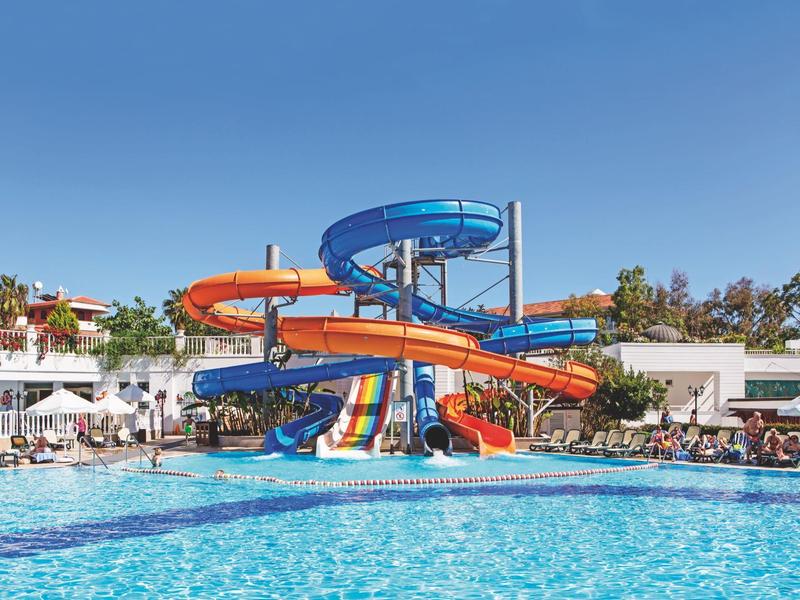 Velký bazén s barevnou skluzavkou a lehátky za slunečného počasí.