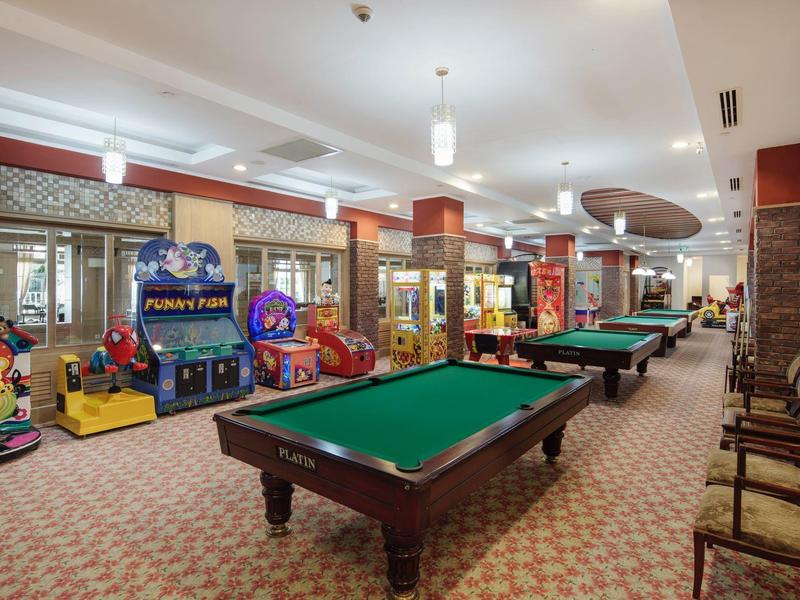 Velká herna s kulečníkovými stoly a herními automaty, útulné prostředí.