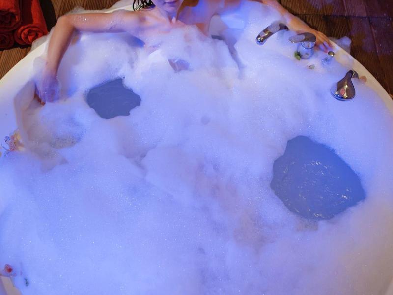 Žena relaxuje v vaně plné pěny s dekorací z mušlí.