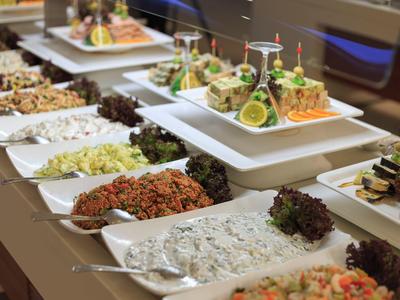 Buffet mit verschiedenen Salaten und kalt zubereiteten Speisen in weißen Schalen auf einer Theke.