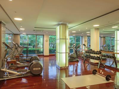 Moderner Fitnessraum mit Holzboden, Gewichten, Laufbändern und großen Fenstern mit Sicht ins Grüne.