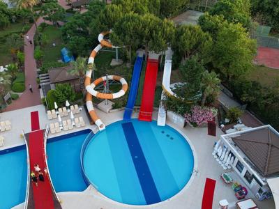 Wasserrutsche und rundes Becken umgeben von Liegestühlen und Bäumen in einer Freizeitbad-Anlage.