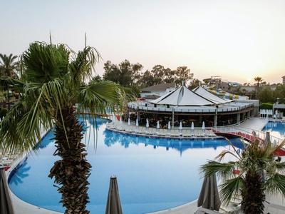 Großer runder Pool mit Bar, umgeben von Palmen und Liegestühlen im Abendlicht.