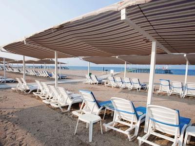 Reihe leerer Sonnenliegen unter gestreiften Sonnenschirmen auf sandigem Strand bei bewölktem Himmel.