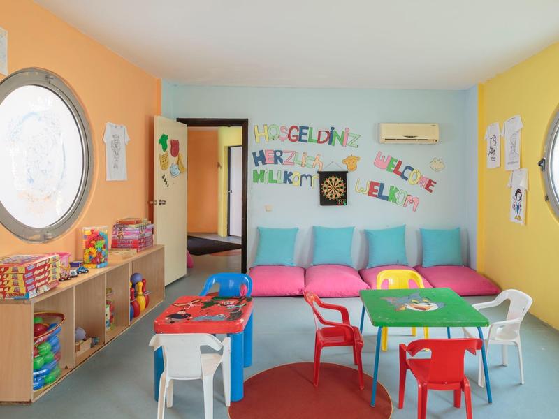 Buntes Kinderspielzimmer mit bunten Stühlen, Tischen, Spielzeugen und Fenster mit Blick nach draußen.
