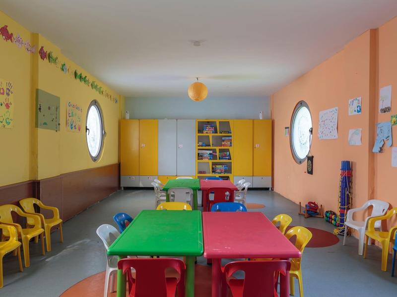 Bunter Kinderraum mit kleinen Stühlen und Tischen, Wänden mit Zeichnungen und gelben Schränken.