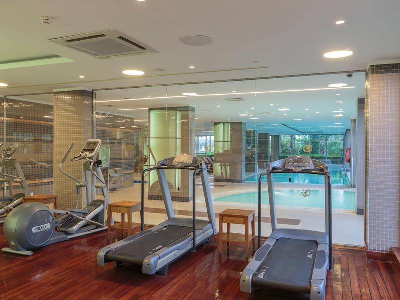 Moderner Fitnessraum mit Laufbändern, Trainingsgeräten und Blick auf einen Innenpool.