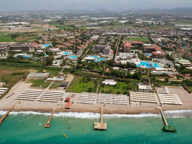 Strand mit mehreren Holzstegen, dahinter Stadt mit vielen Gebäuden und weiter entfernten Bergen.