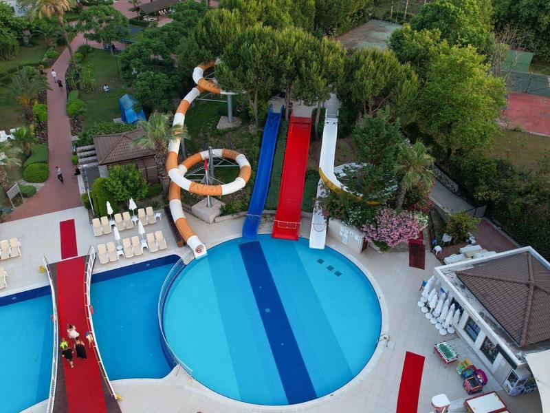 Wasserrutsche und rundes Becken umgeben von Liegestühlen und Bäumen in einer Freizeitbad-Anlage.